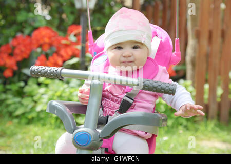 Adorable 6 months old little girl on pink tricycle in garden Stock Photo