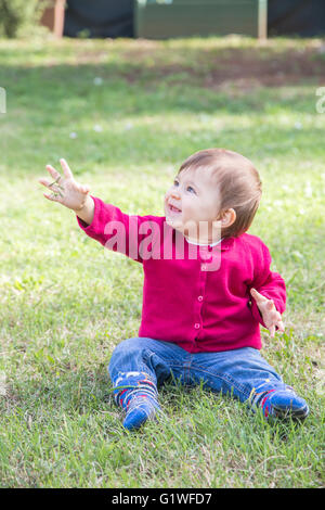 One year old baby girl sitting on grass while smiling with grass in hand Stock Photo
