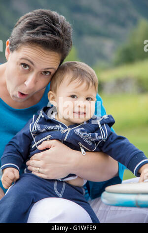 Funny mother making faces to camera while holding lovely one year old baby Stock Photo