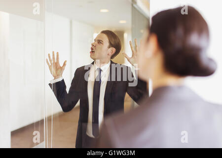 Silly businessman pressing face against office glass Stock Photo