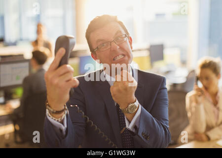 Furious businessman gesturing with fist at telephone in office Stock Photo