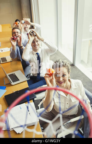 Business people aiming plastic balls at basketball hoop in conference room Stock Photo