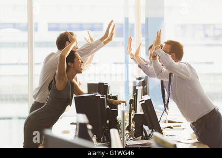 Exuberant business people high-fiving over computers in office Stock Photo