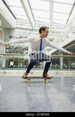 Playful businessman skateboarding in office corridor Stock Photo