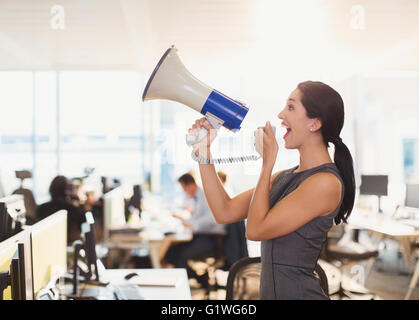 Exuberant businesswoman using megaphone in office Stock Photo