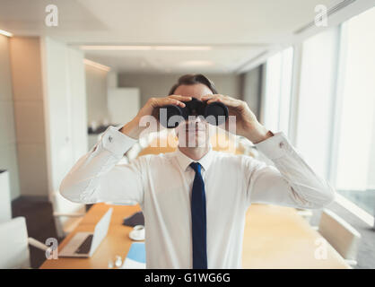 Portrait of businessman using binoculars in conference room Stock Photo