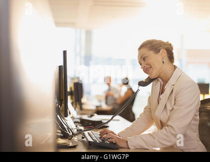 Smiling businesswoman talking on telephone and working at computer in office Stock Photo