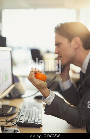 Angry businessman squeezing stress ball and talking on telephone at computer in office Stock Photo