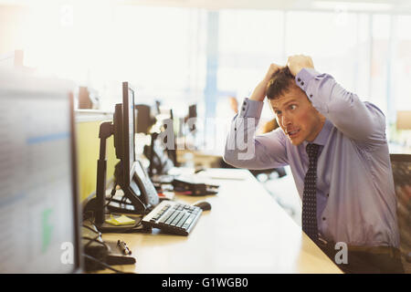 Stressed businessman pulling his hair out at computer in office Stock Photo