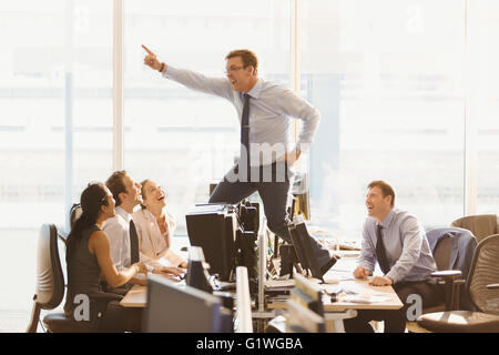 Laughing colleagues watching exuberant businessman dancing on top of desks in office Stock Photo