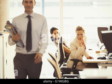 Businesswomen checking out passing businessman in office Stock Photo