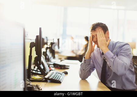 Stressed businessman with head in hands at office desk Stock Photo