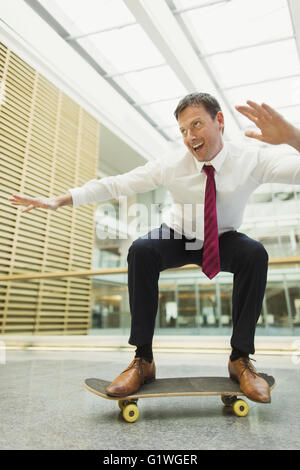 Playful businessman skateboarding in office Stock Photo