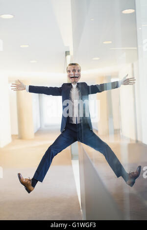 Symmetrical reflection portrait of businessman with arms and legs outstretched in office corridor Stock Photo