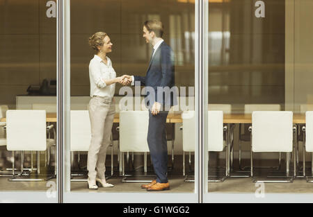 Businessman and businesswoman handshaking at conference room window Stock Photo