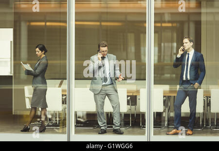 Business people on cell phones and taking notes at conference room window Stock Photo