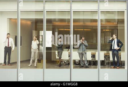 Business people talking on cell phones and reviewing paperwork at conference room window Stock Photo