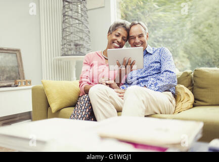 Smiling mature couple using digital tablet on living room sofa Stock Photo