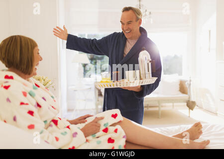 Enthusiastic mature man serving breakfast to wife in bed Stock Photo