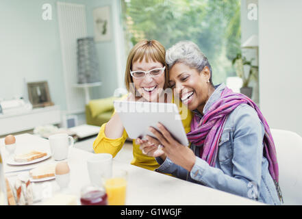 Laughing mature women sharing digital tablet at breakfast table Stock Photo