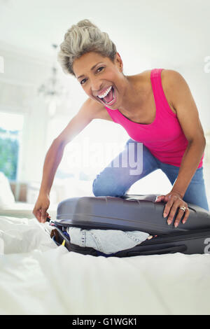 Portrait enthusiastic mature woman closing suitcase on bed Stock Photo