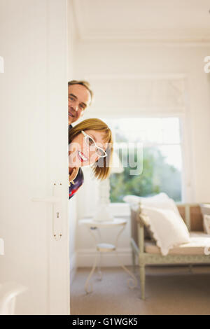 Portrait playful mature couple peering from behind door Stock Photo