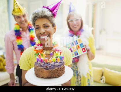Portrait smiling mature woman holding chocolate birthday cake with friends in background Stock Photo