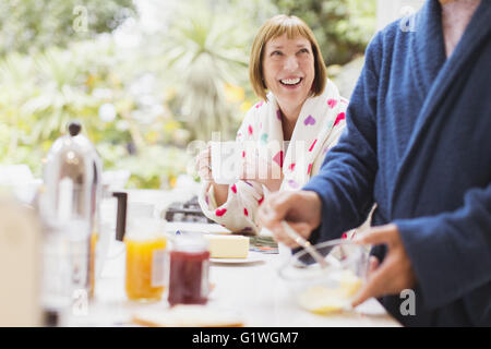 Smiling mature woman drinking coffee in bathrobe at breakfast Stock Photo