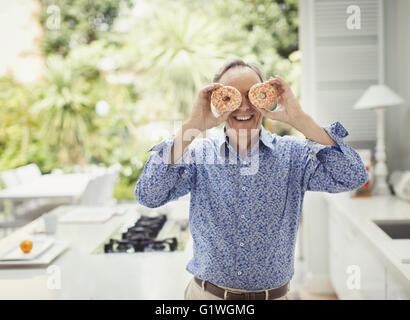 Portrait playful mature man covering eyes with donuts Stock Photo