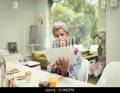 Smiling mature woman using digital tablet at breakfast table Stock Photo