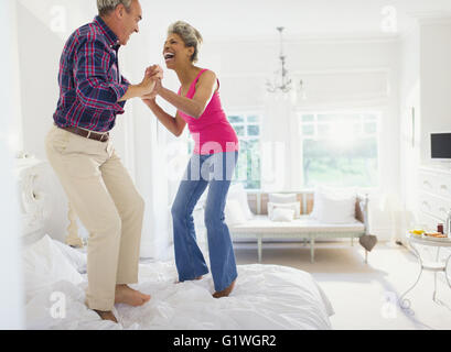 Playful mature couple jumping on top of bed Stock Photo