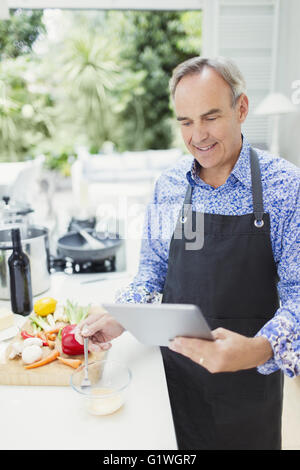 Mature man in apron using digital tablet cooking in kitchen Stock Photo