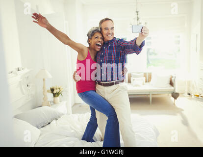 Playful mature couple taking selfie standing on bed