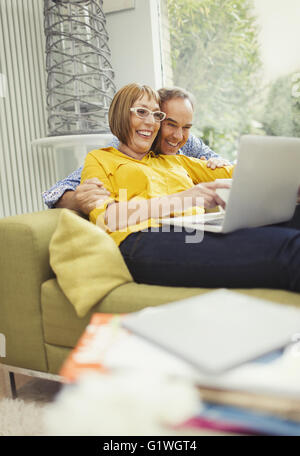 Smiling mature couple sharing laptop on living room sofa Stock Photo