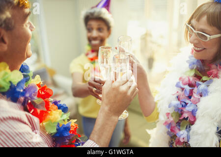 Playful mature friends in feather boas and leis toasting champagne flutes Stock Photo