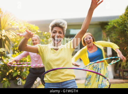 Portrait playful mature adults spinning with plastic hoops in garden Stock Photo