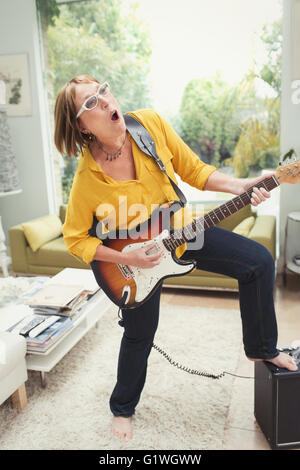 Playful mature woman playing electric guitar in living room Stock Photo