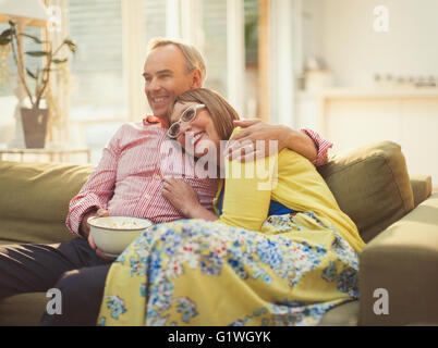 Affectionate mature couple watching TV and eating popcorn on living room sofa Stock Photo