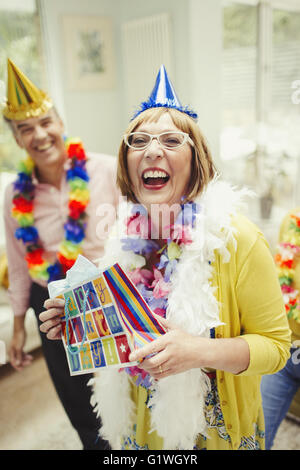 Portrait laughing mature woman in party hat holding birthday gift Stock Photo