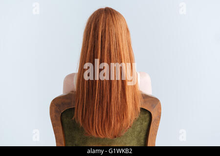 Rear view portrait of a redhead woman sitting on the chair isolated on a white background Stock Photo