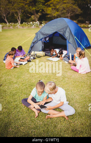 Smiling children are looking their tablet with other children behind them Stock Photo