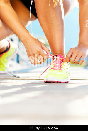 Running shoes - woman tying shoe laces. Closeup of female sport fitness runner getting ready for jogging outdoors on waterfront Stock Photo