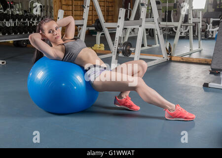 A muscular young women working out (or exercising) in a gym with an exercise ball Stock Photo