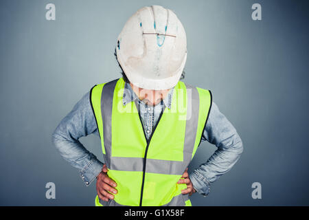 A young engineer in hard hat and high vis is looking down Stock Photo