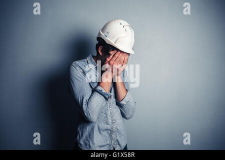 An upset blue collar worker is burying his face in his hands Stock Photo