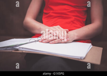 A young woman is sitting on a sofa with a ring binder filled with documents Stock Photo