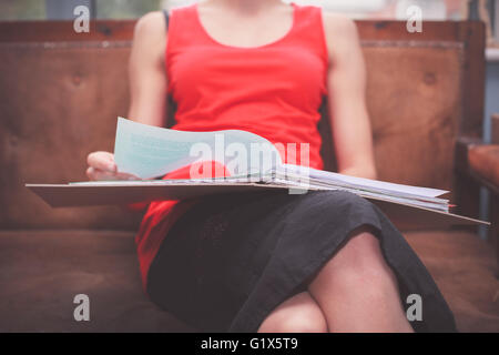A young woman is sitting on a sofa with a ring binder filled with documents Stock Photo