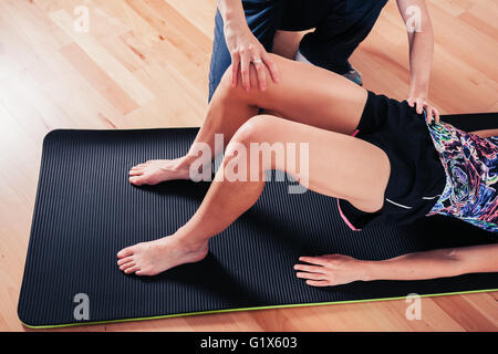 A therapist is correcting the technique of a woman exercising and stretching in a gym Stock Photo
