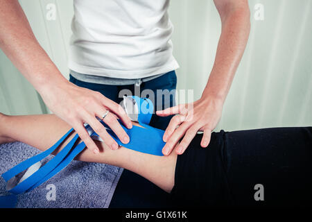 A physiotherapist is applying kinesio tape to a patient's leg Stock Photo