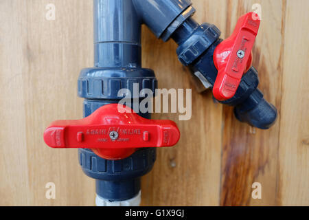 Bright red valves on PVC water pipes against a wooden backdrop. Stock Photo